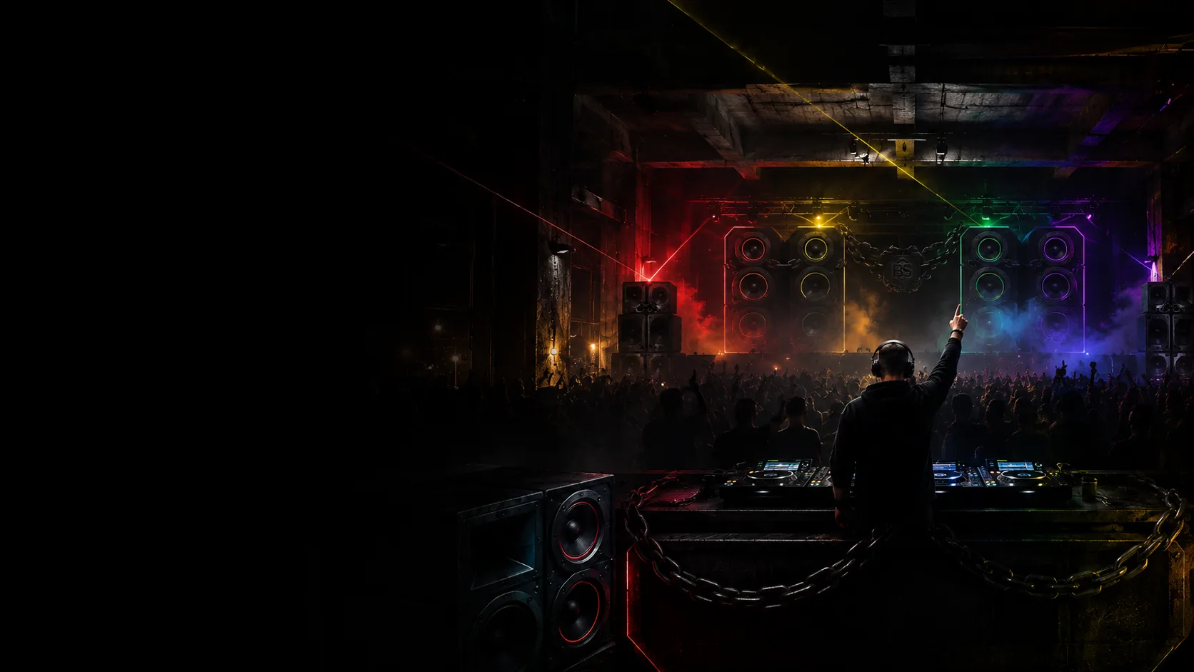 DJ with one hand raised above the decks as a warehouse crowd goes up under coloured lasers